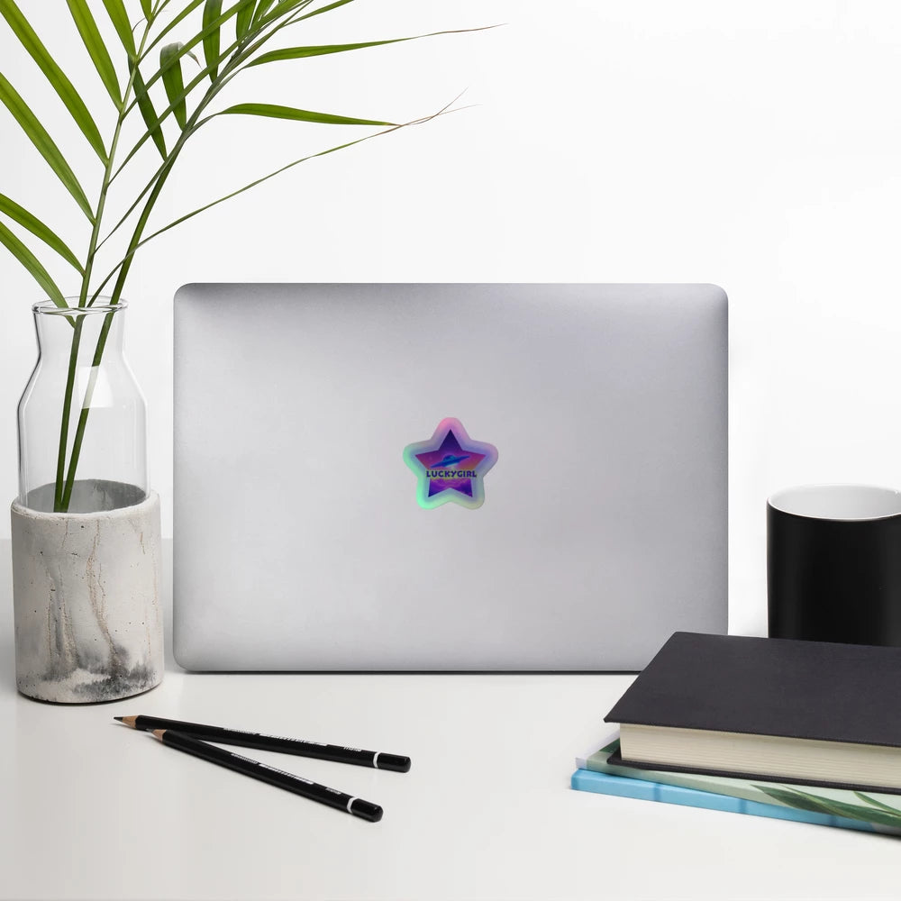 Laptop with a colorful star sticker on a desk with a plant, notebook, and pens.